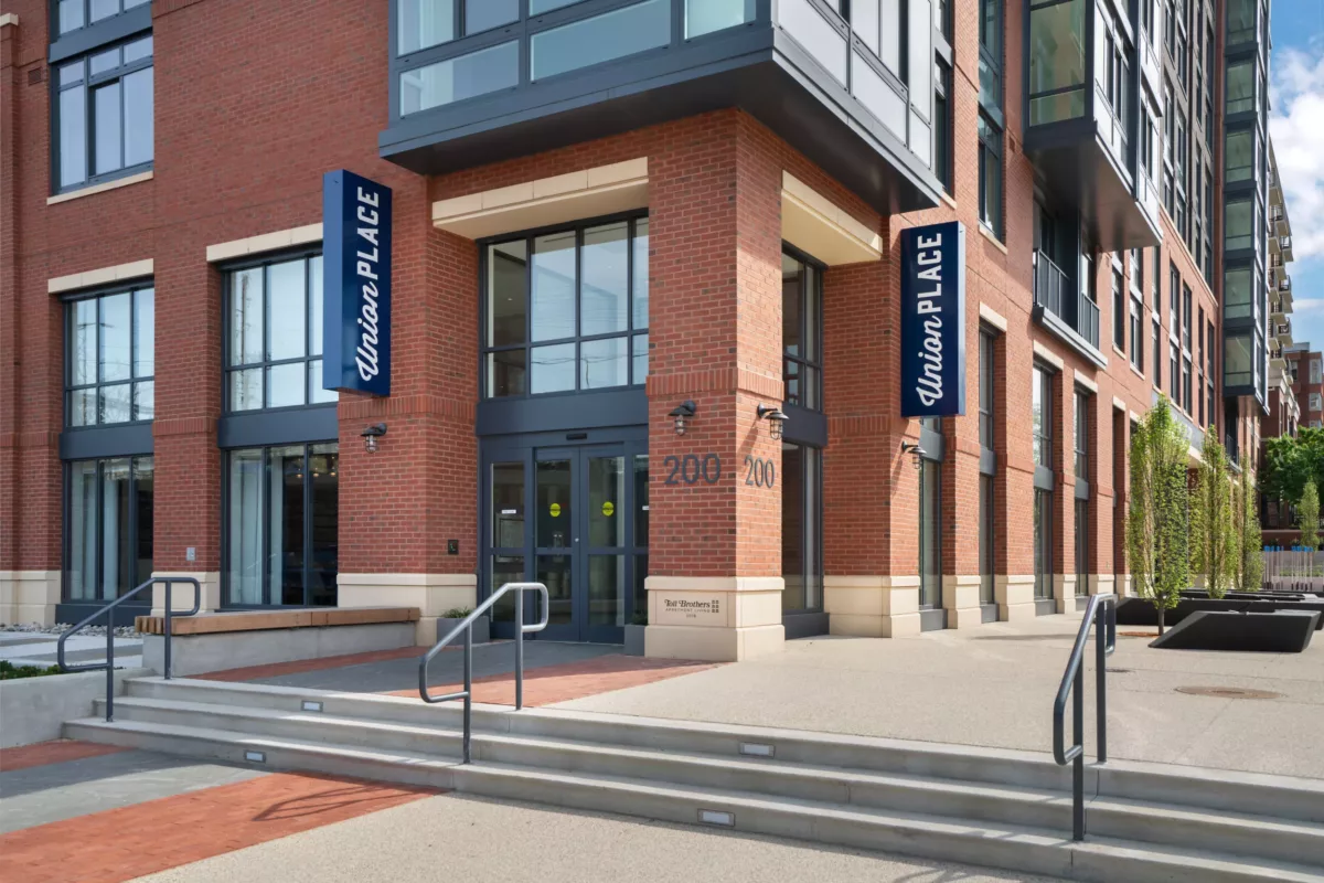 Apartment building main entrance with steps, glass doors, and branded signage.