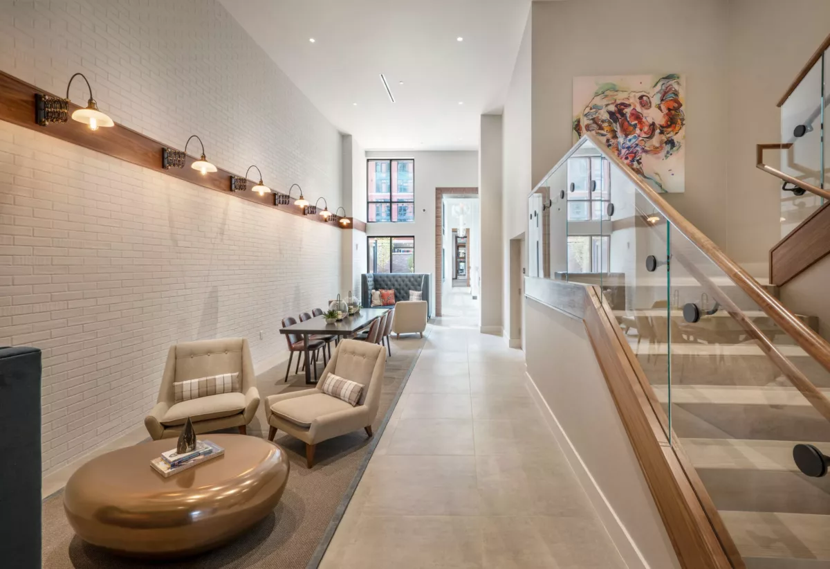 Modern lobby seating area with lounge chairs, wall lighting, and staircase with glass railing.