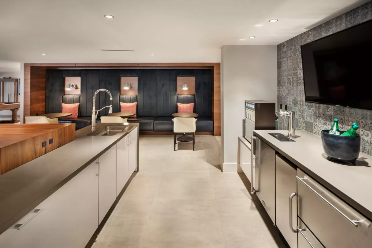 Community kitchen and lounge with large island, stainless appliances, built-in seating, and wall-mounted TV.