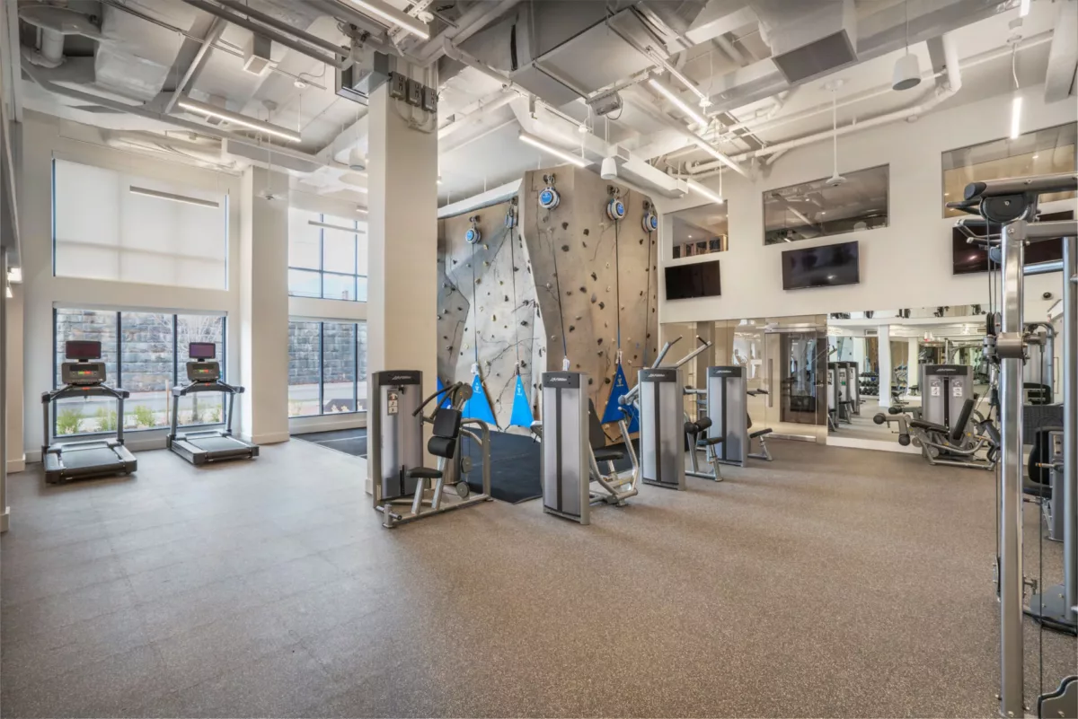 Spacious gym with cardio equipment, strength machines, and exposed ceilings.