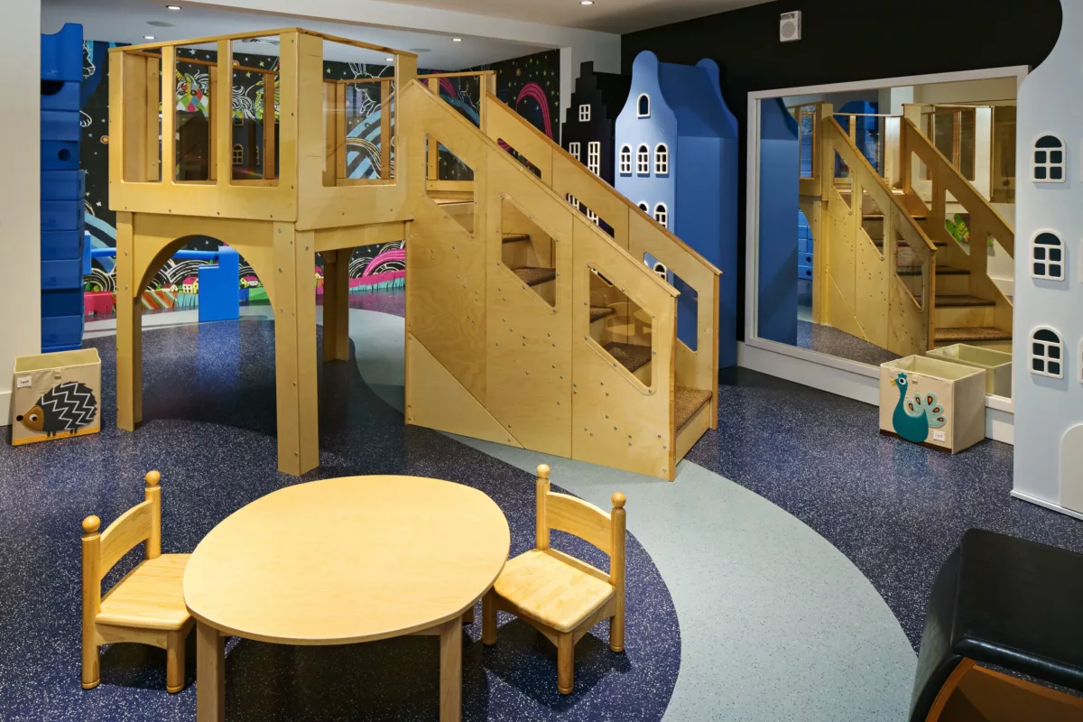 Children’s playroom with wooden climbing structure, stairs, small table, and colorful wall décor.