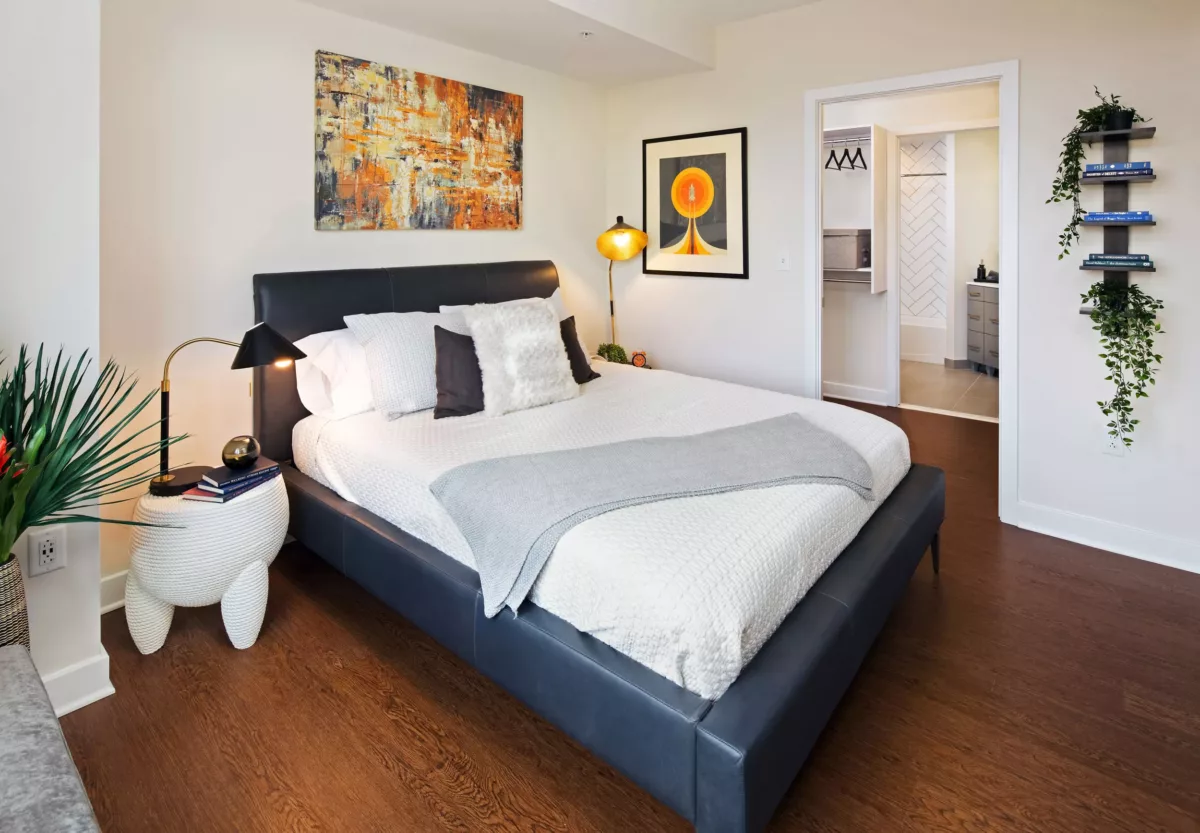 Bright bedroom with upholstered bed, accent art, and hardwood flooring.
