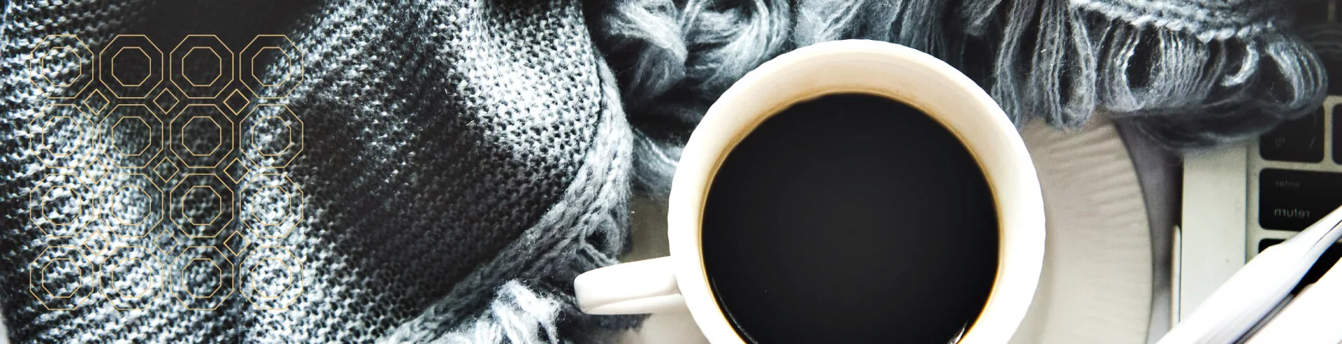 close up of a full coffee cup on saucer surrounded by gray/blue blanket